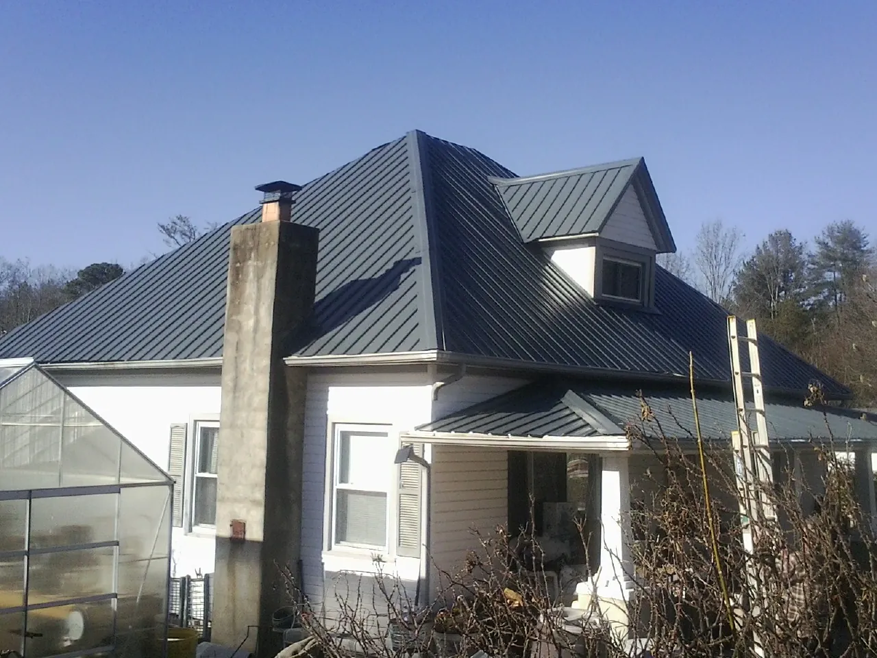 Dark blue standing seam metal roof on a white farmhouse with dormer — Slate & Tile Roof Repair by Roofing Brothers in Easley