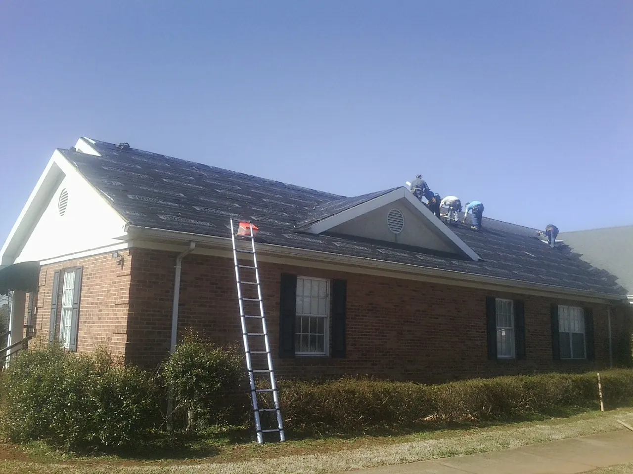 Crew tearing shingles off a brick ranch roof with a ladder set — Metal Roof Repair work by our crew in Easley
