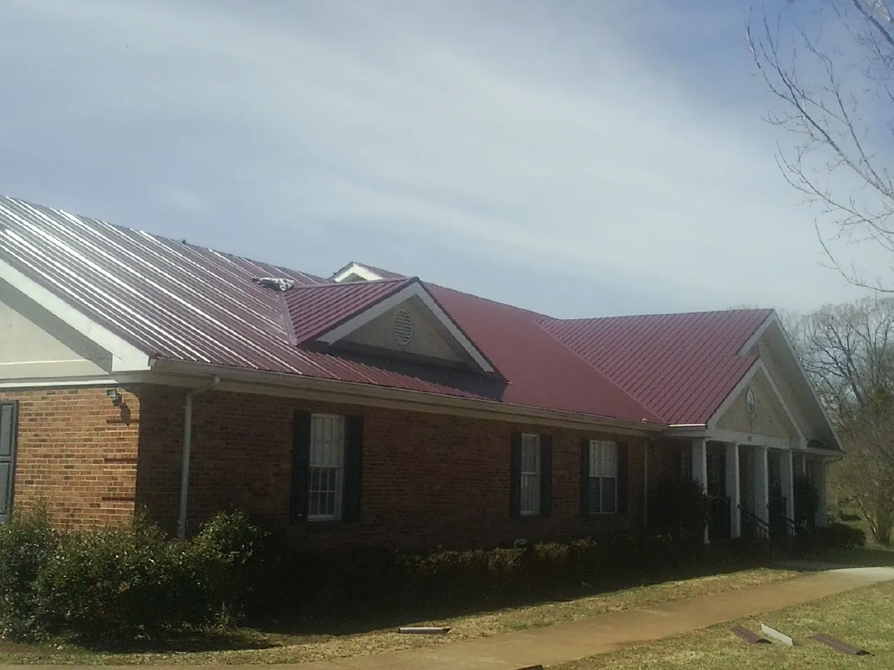 Red metal roof with gabled entries on a long brick building, from a Hail Damage Roof Repair job in Easley