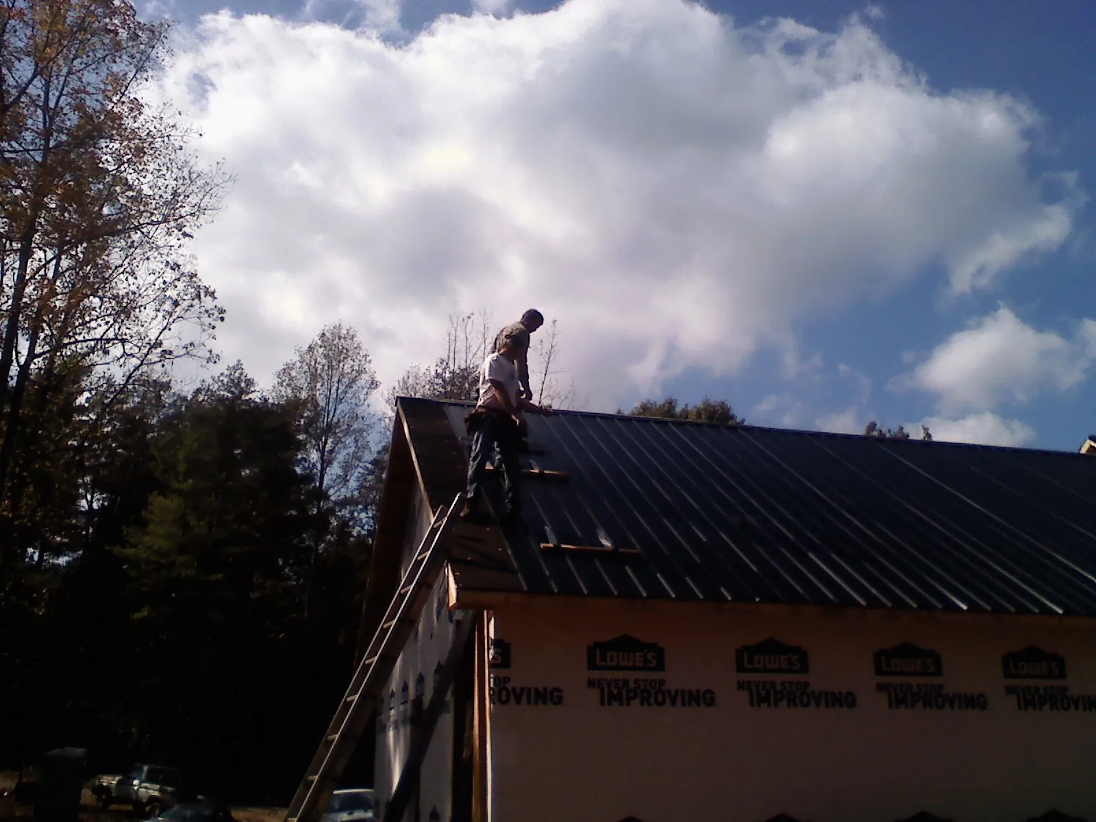 Roofer fastening dark metal panels high against a cloudy sky, from a Roof Inspection job in Easley