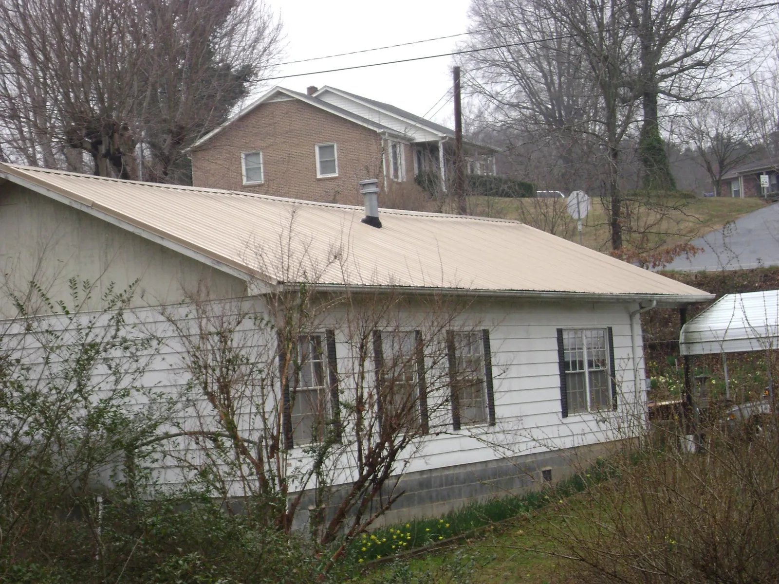 Tan metal roof on a white sided house set into a hillside — Commercial Roofing by Roofing Brothers in Easley